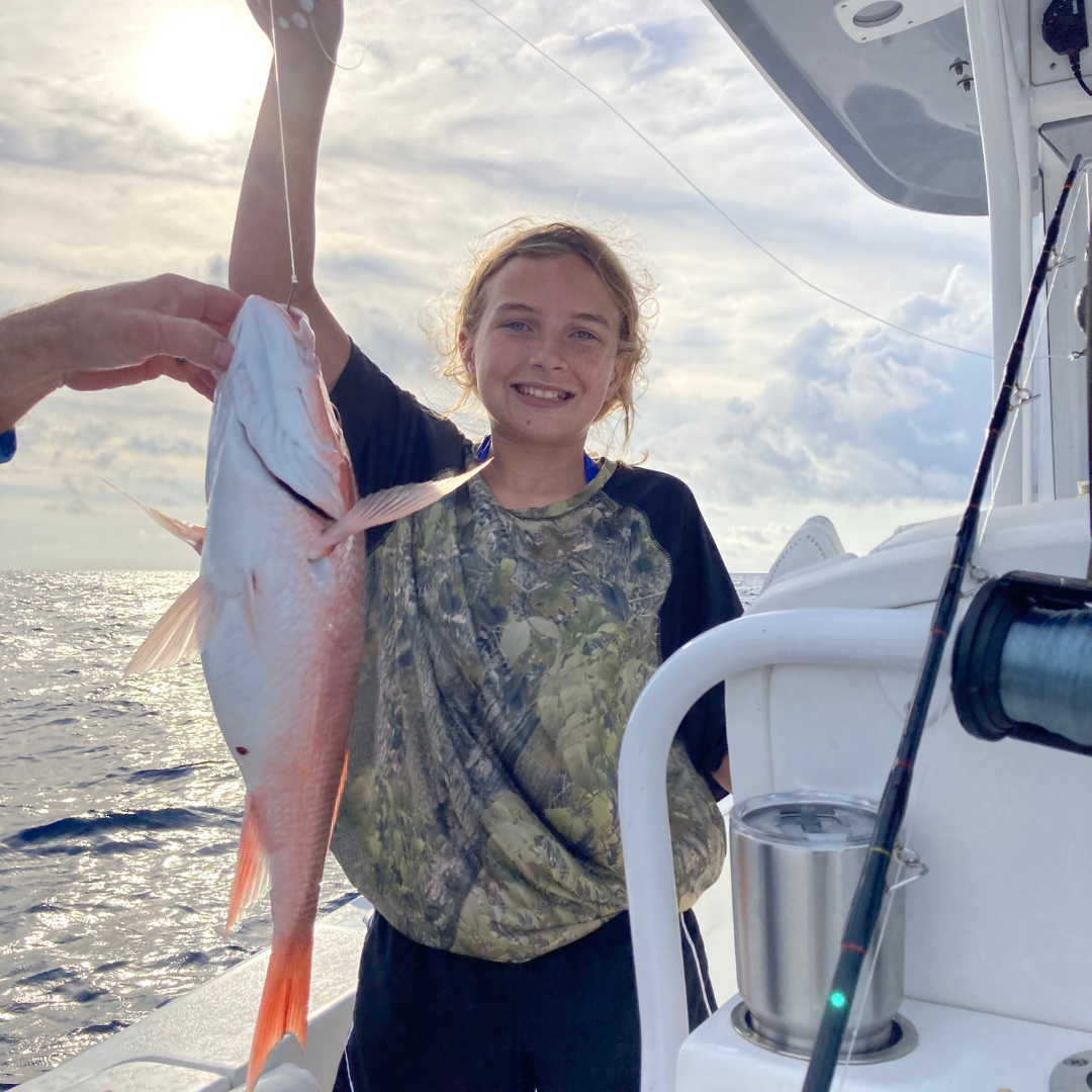 Child holding a fish on a boat at sunset
