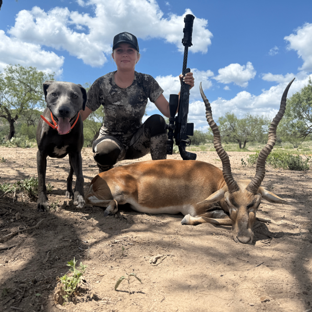 Woman hunter and dog beside a harvested antelope under a bright blue sky