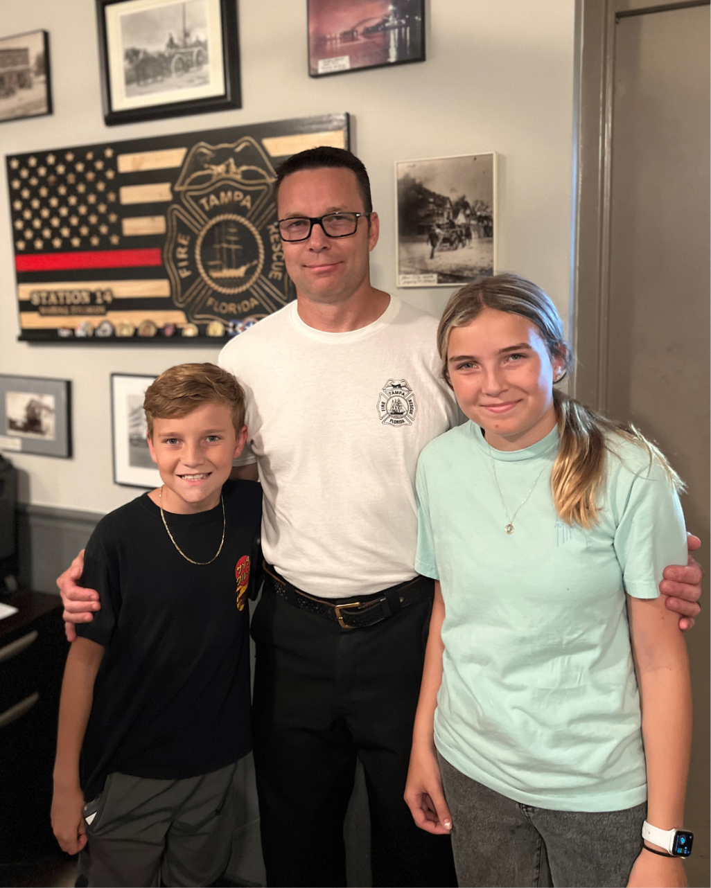 Father in a Tampa Fire Rescue shirt standing with his son and daughter at the firehouse