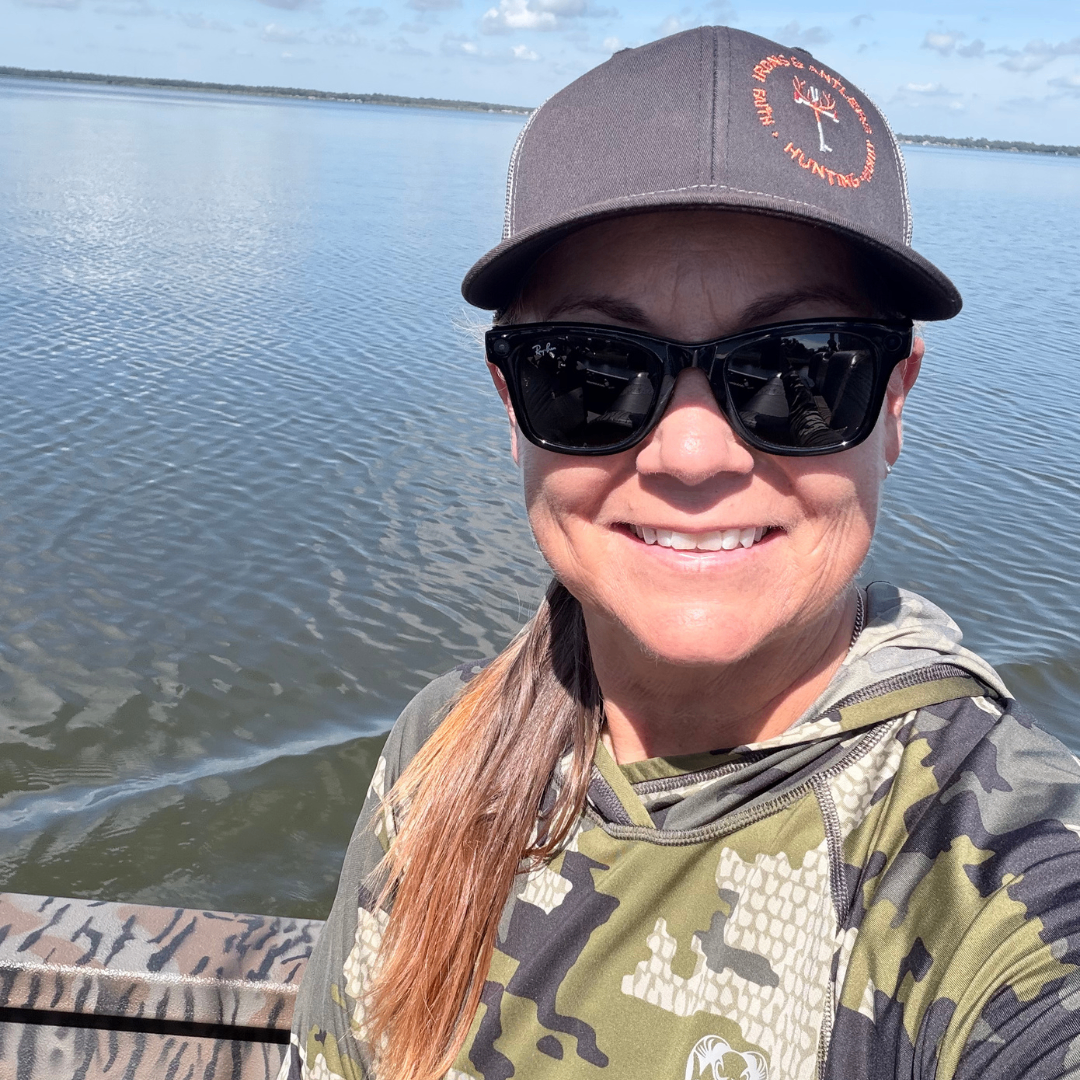 Woman wearing Irons and Antlers gear smiling from a boat on a calm lake