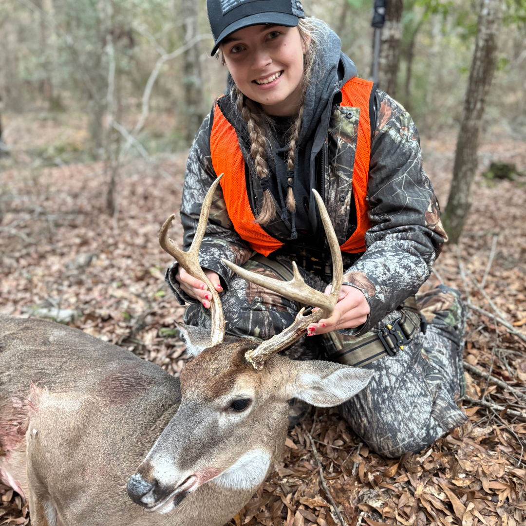 Young woman kneeling beside a harvested deer in the woods