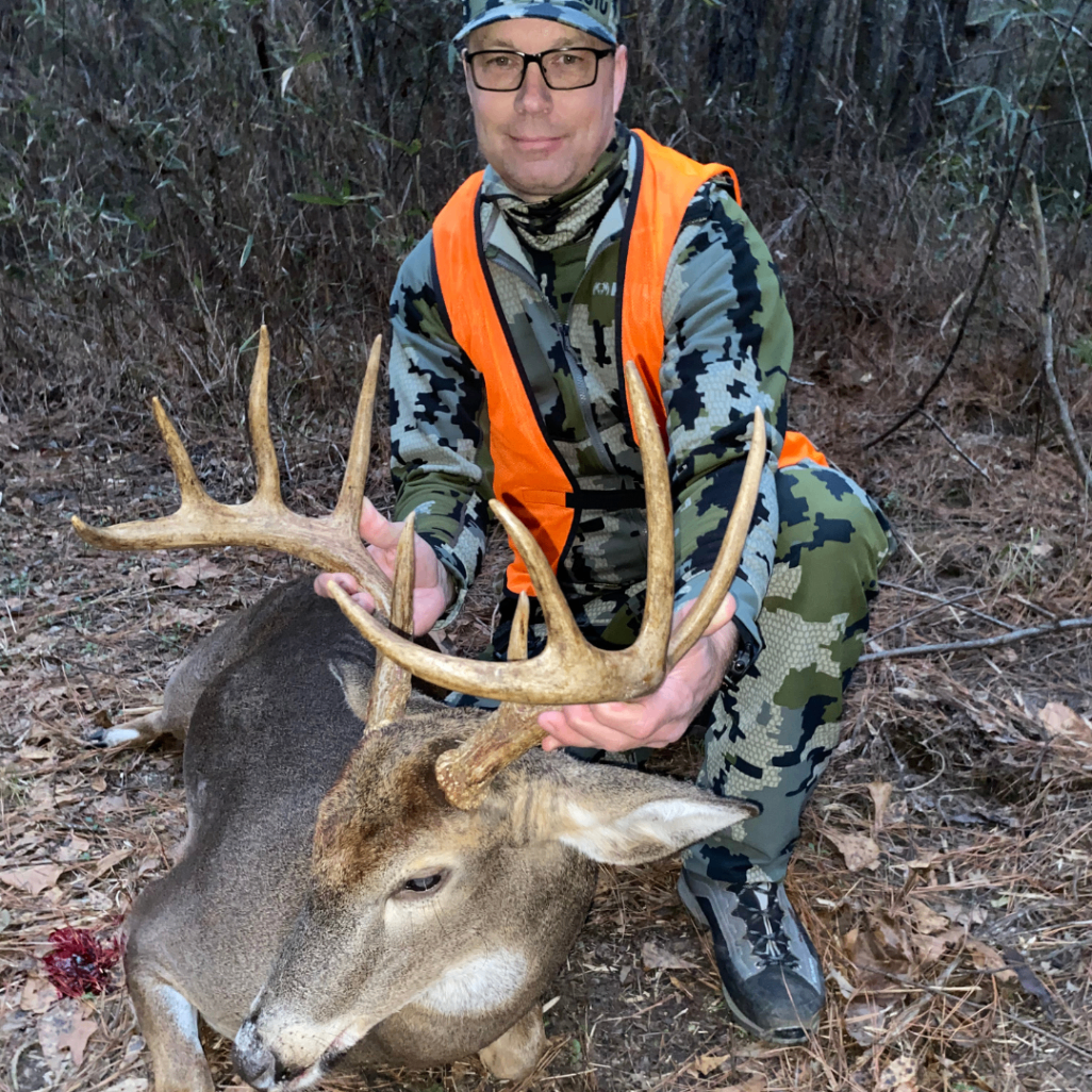 Hunter in camouflage kneeling beside a harvested buck