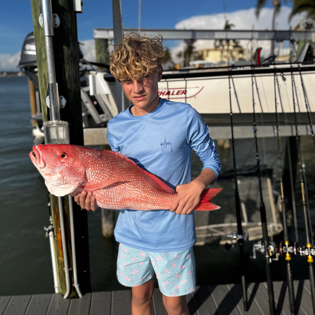 Boy holding a large red fish beside a boat