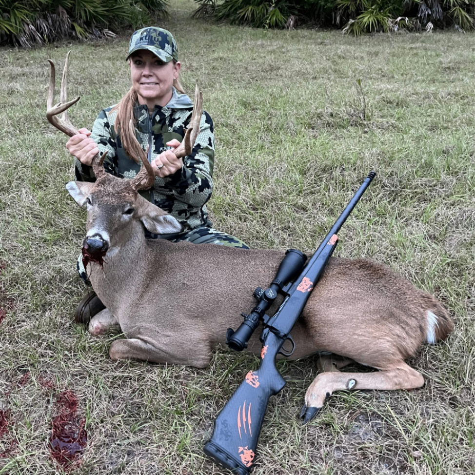 Woman hunter kneeling behind a harvested whitetail deer in a grassy field